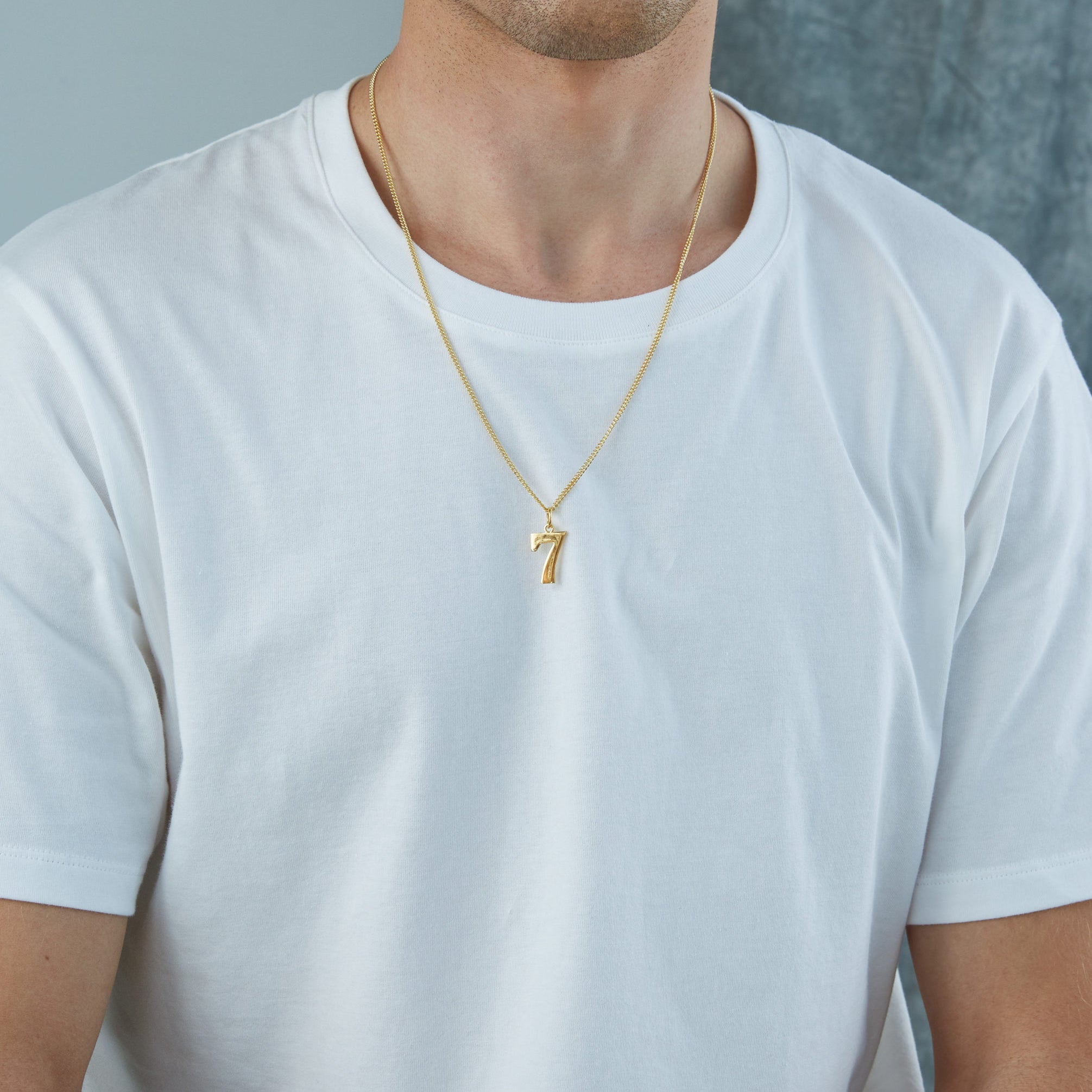 Man wearing a gold necklace with a small pendant on a plain background - Tilly Sveaas