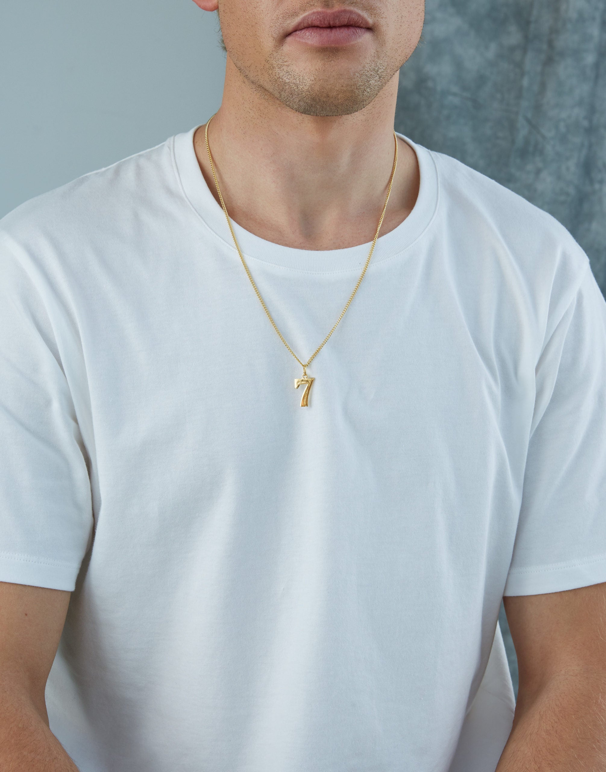 Man wearing a gold necklace with a small pendant on a plain background - Tilly Sveaas