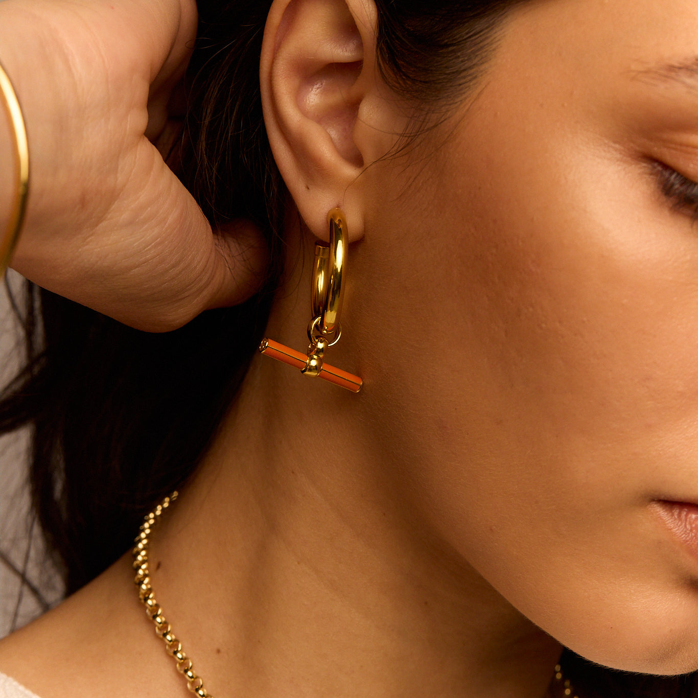 Gold hoop earrings with orange enamel bar charm on the front