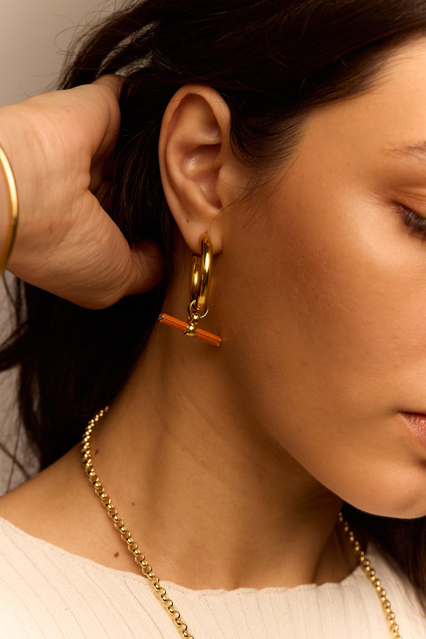 Gold hoop earrings with orange enamel bar charm on the front