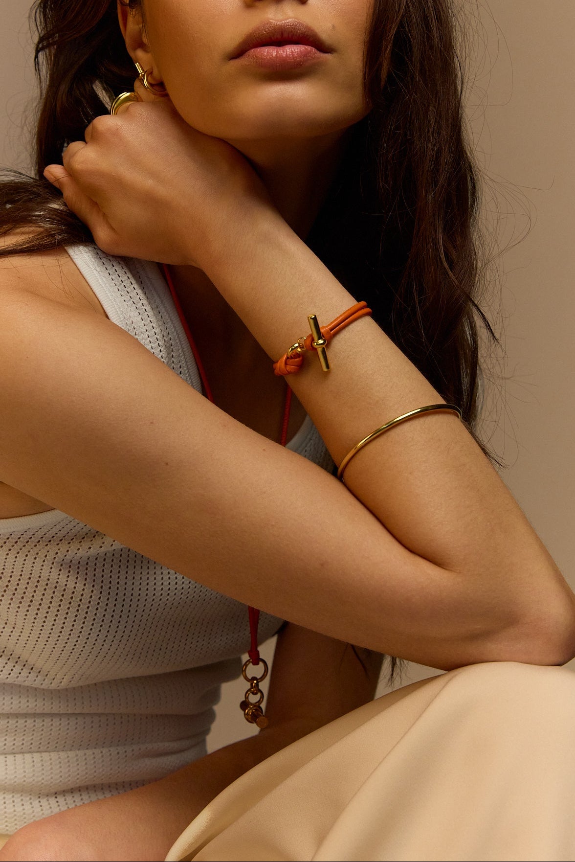 Orange leather T-bar bracelet on wrist with gold cross charm and knot