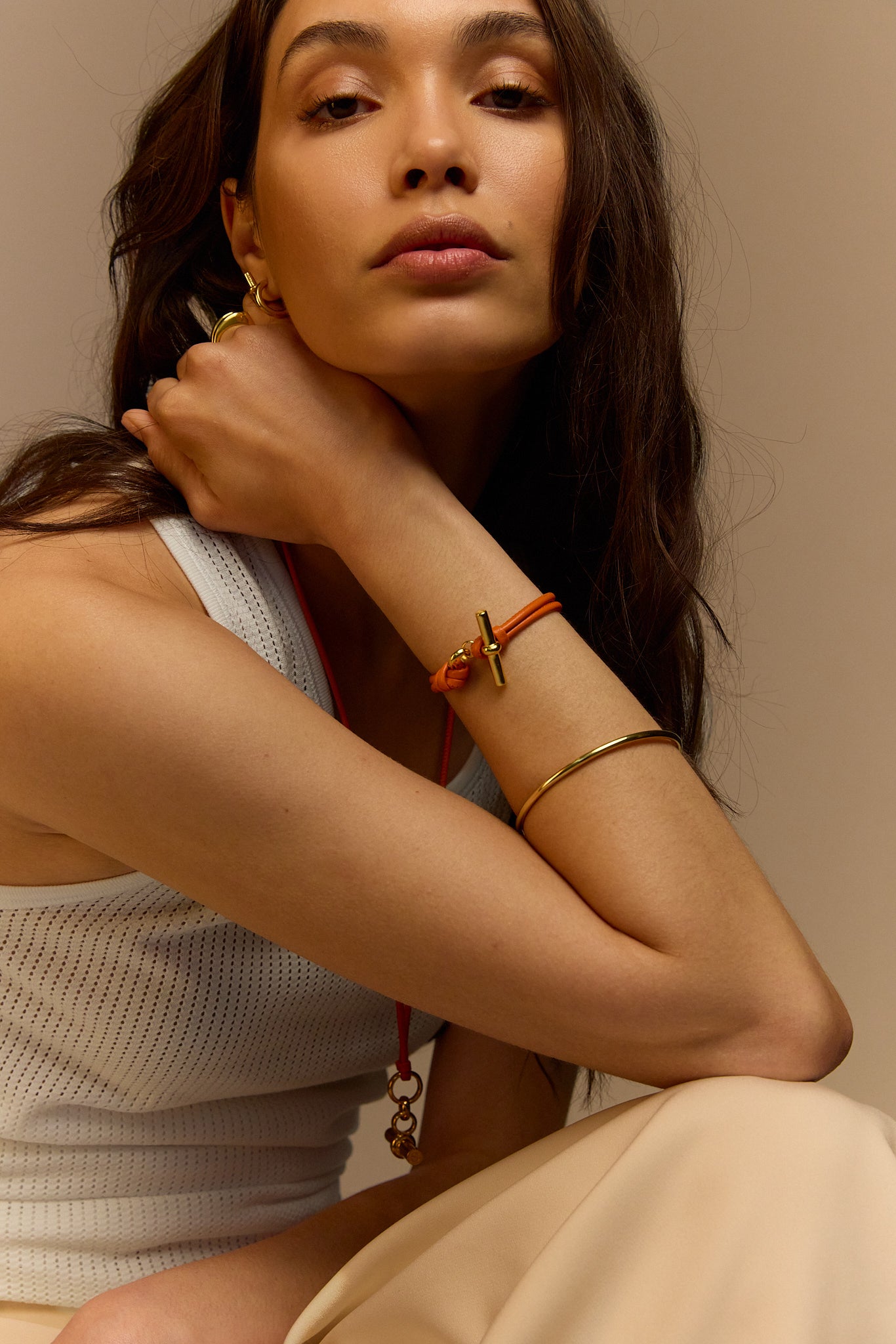 Orange leather T-bar bracelet on wrist with gold cross charm and knot