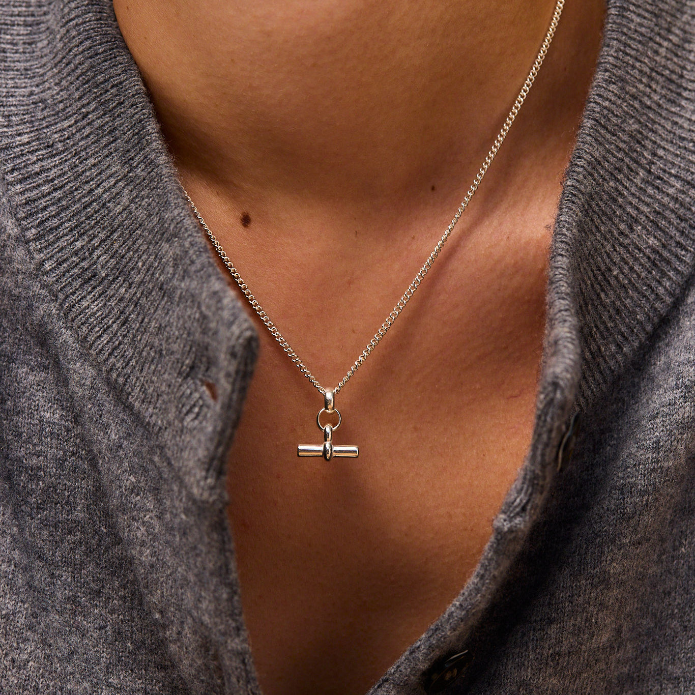 Mini silver T-bar pendant on fine curb chain necklace, centered on neckline