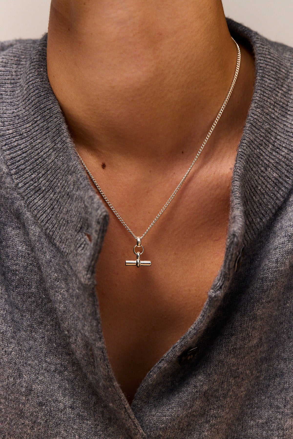 Mini silver T-bar pendant on fine curb chain necklace, centered on neckline