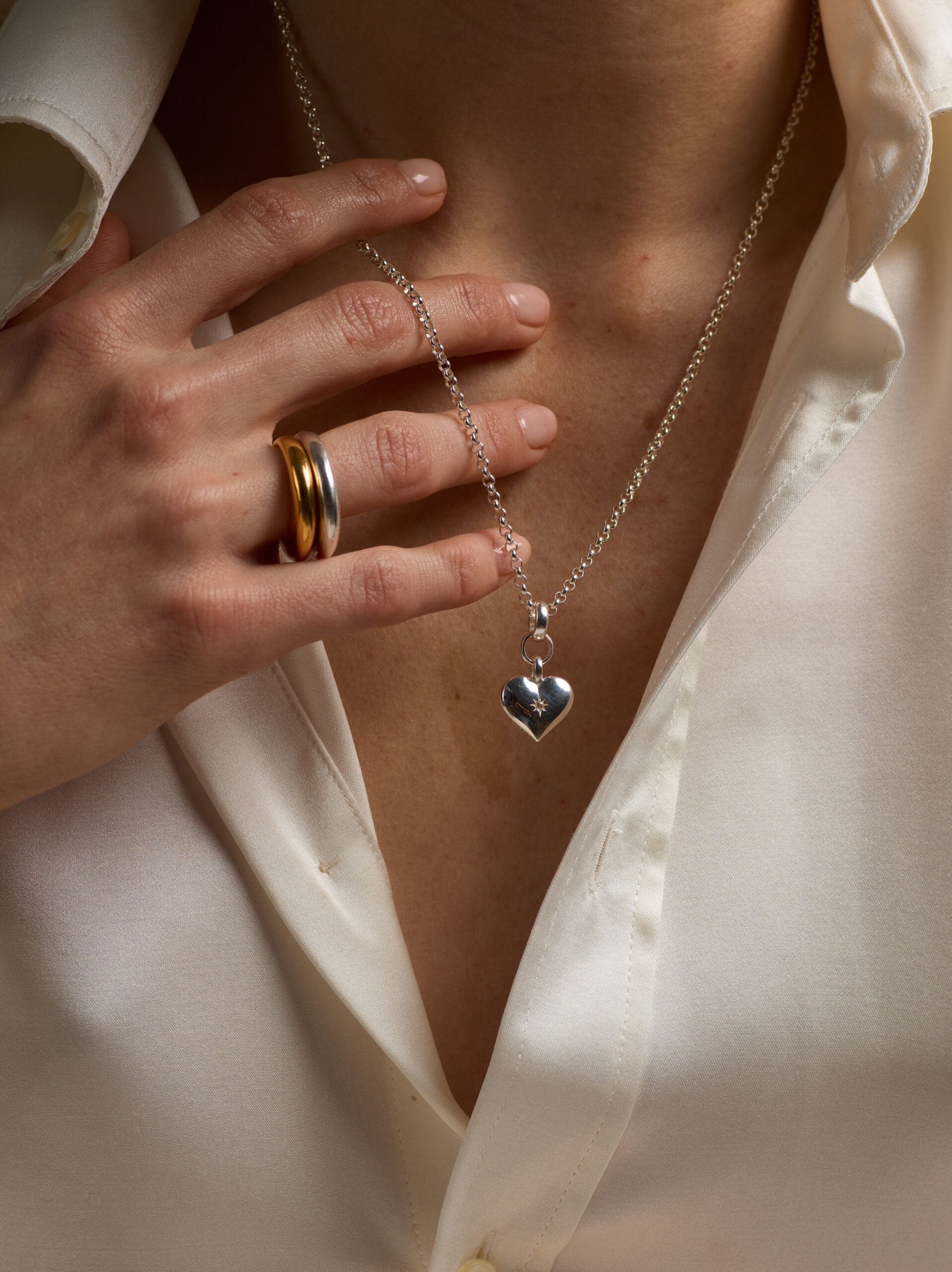 Silver heart pendant necklace worn with long chain; small link texture visible.