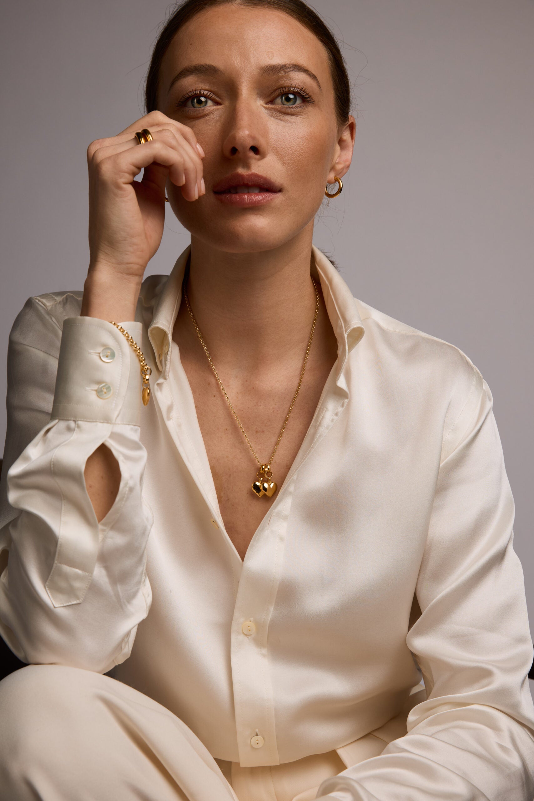Woman wearing a white blouse with cut-out sleeves and a gold necklace against a neutral background