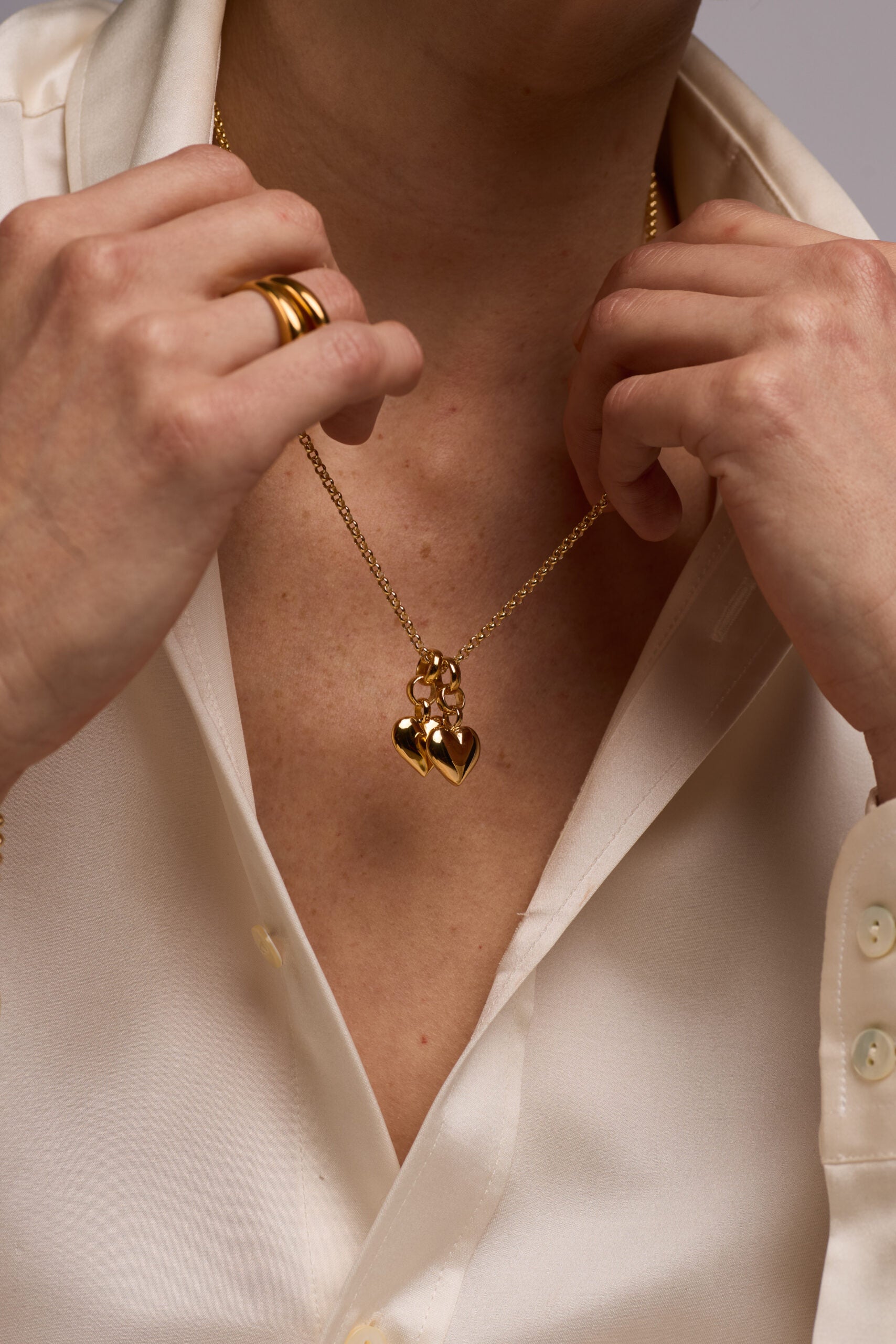 Person wearing a gold necklace with heart pendants, adjusting it with their hands.