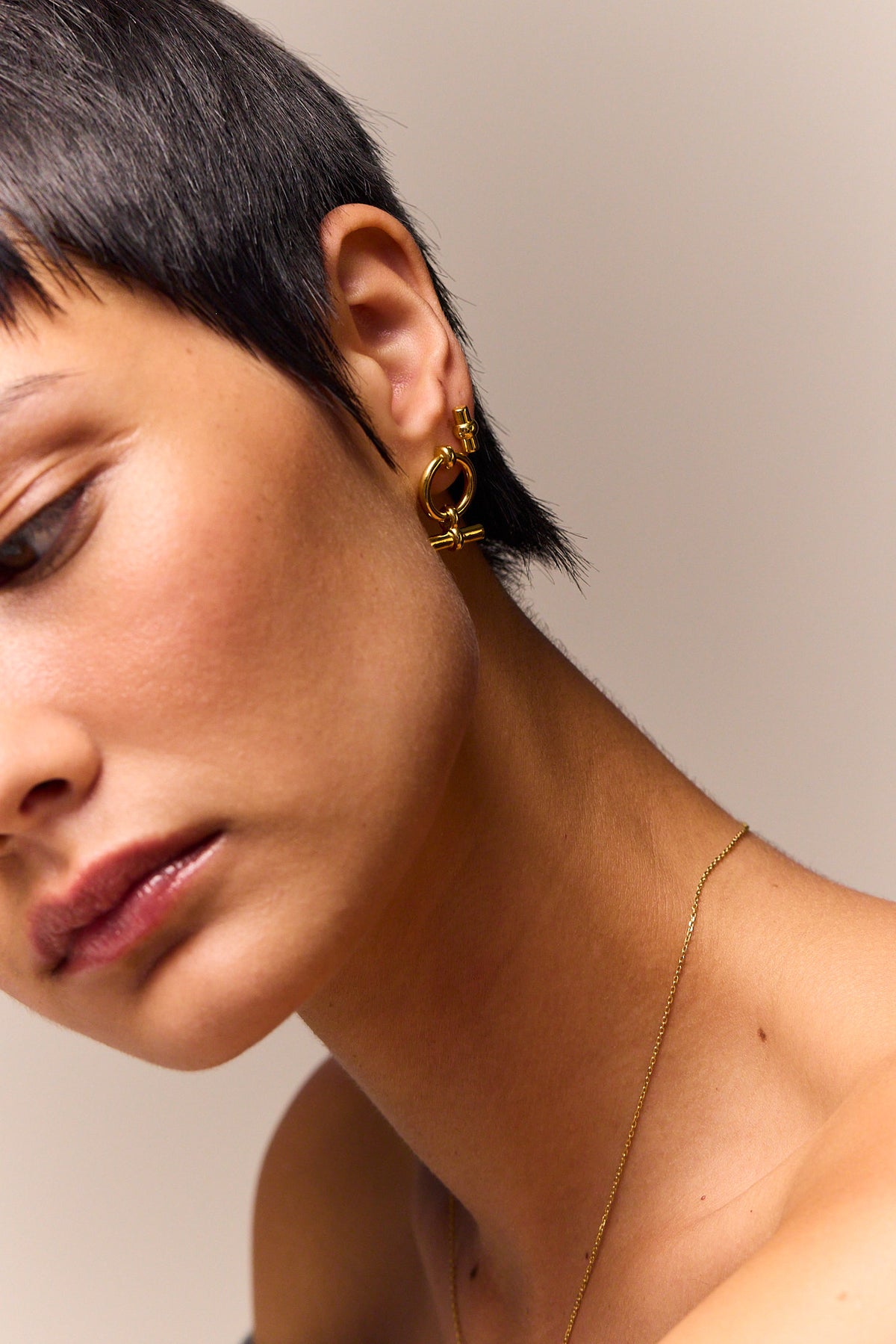 Mini gold hoop stud earrings with T-bar eternity detail, worn on ear
