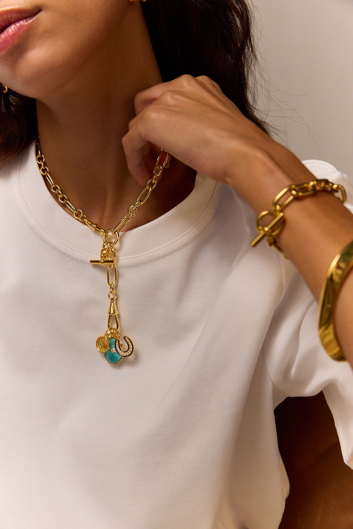 Gold charm necklace with horseshoe pendant and turquoise enamel on a white crewneck