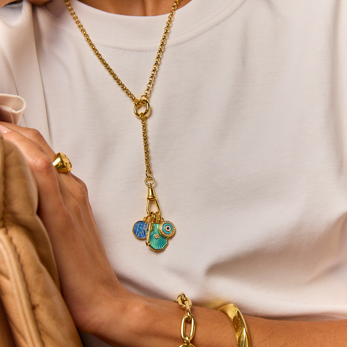 Gold-tone long necklace with blue evil-eye pendant over white top, with gold cuff bracelet
