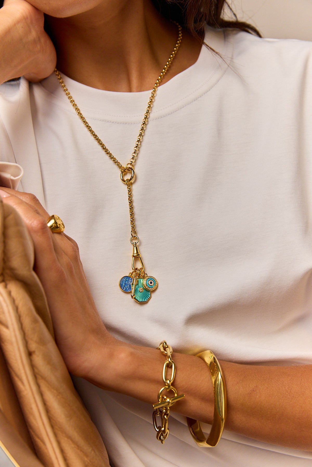 Gold-tone long necklace with blue evil-eye pendant over white top, with gold cuff bracelet