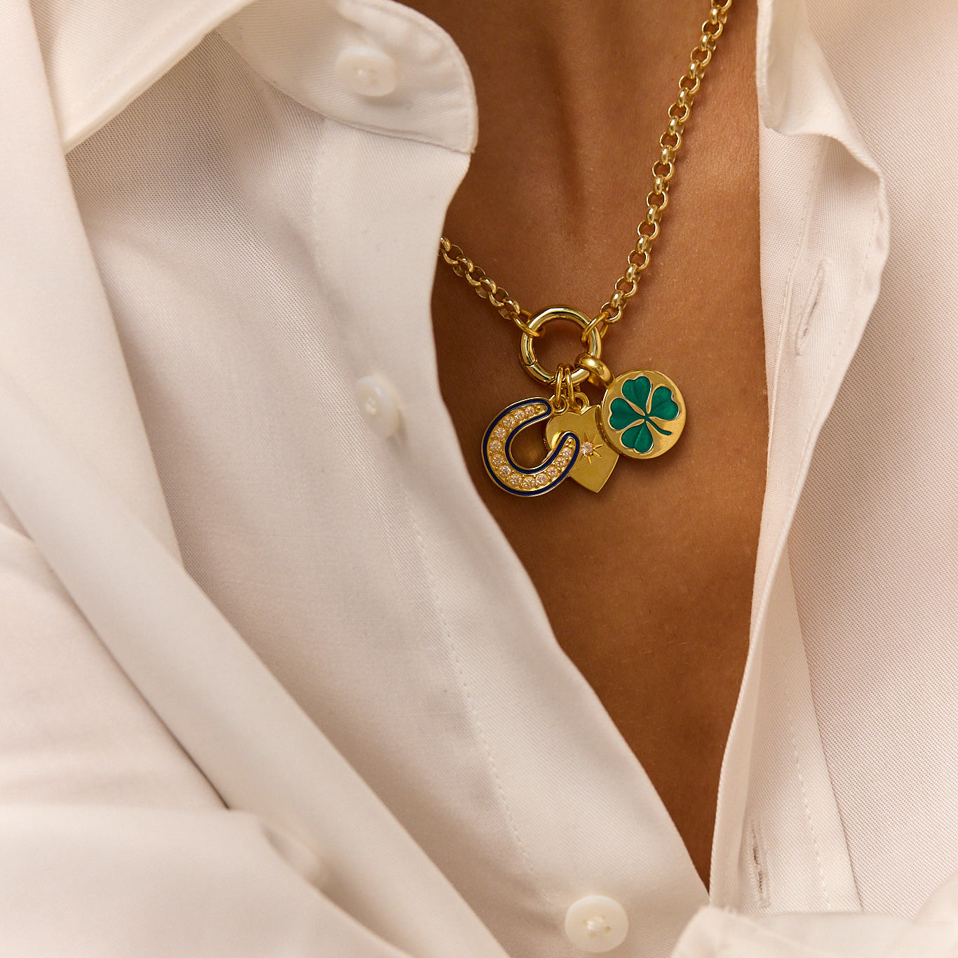 Gold-tone heart and clover charm pendant necklace with green enamel, worn over white shirt
