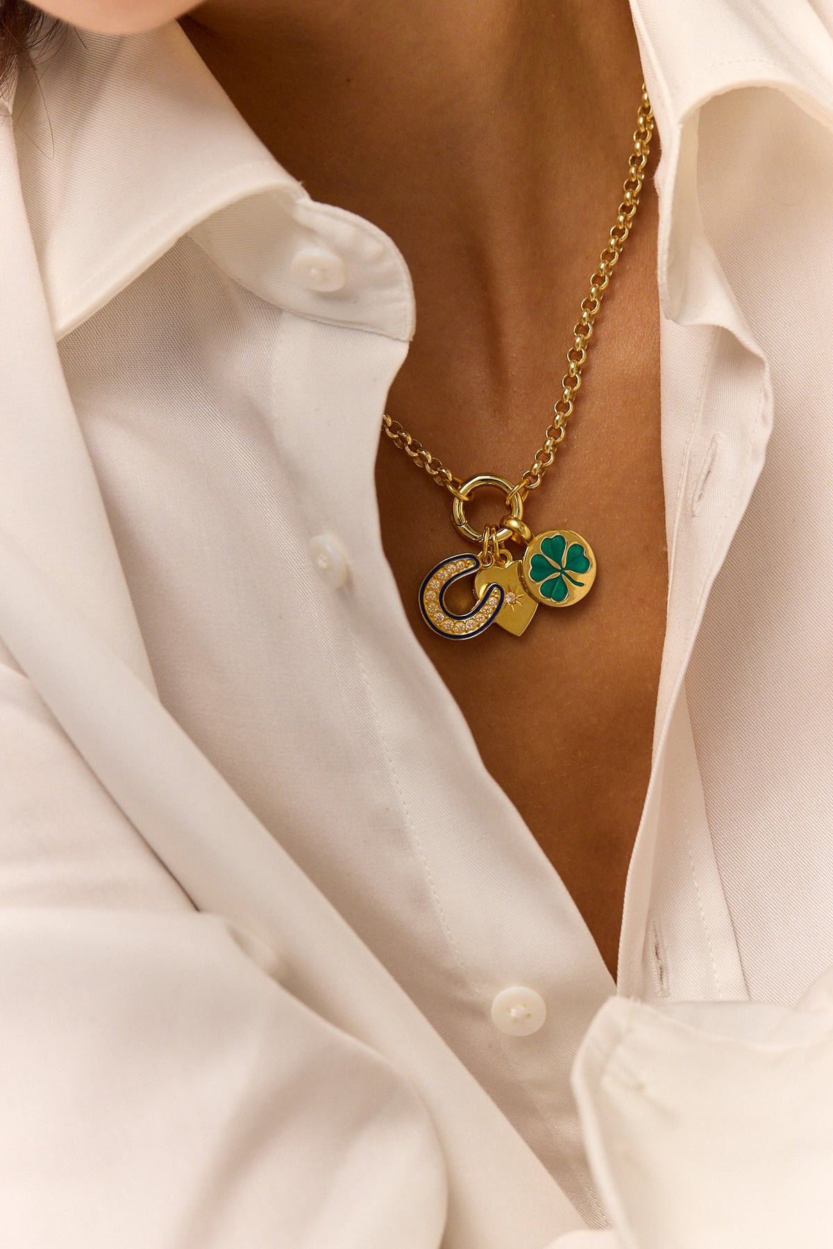 Gold-tone heart and clover charm pendant necklace with green enamel, worn over white shirt