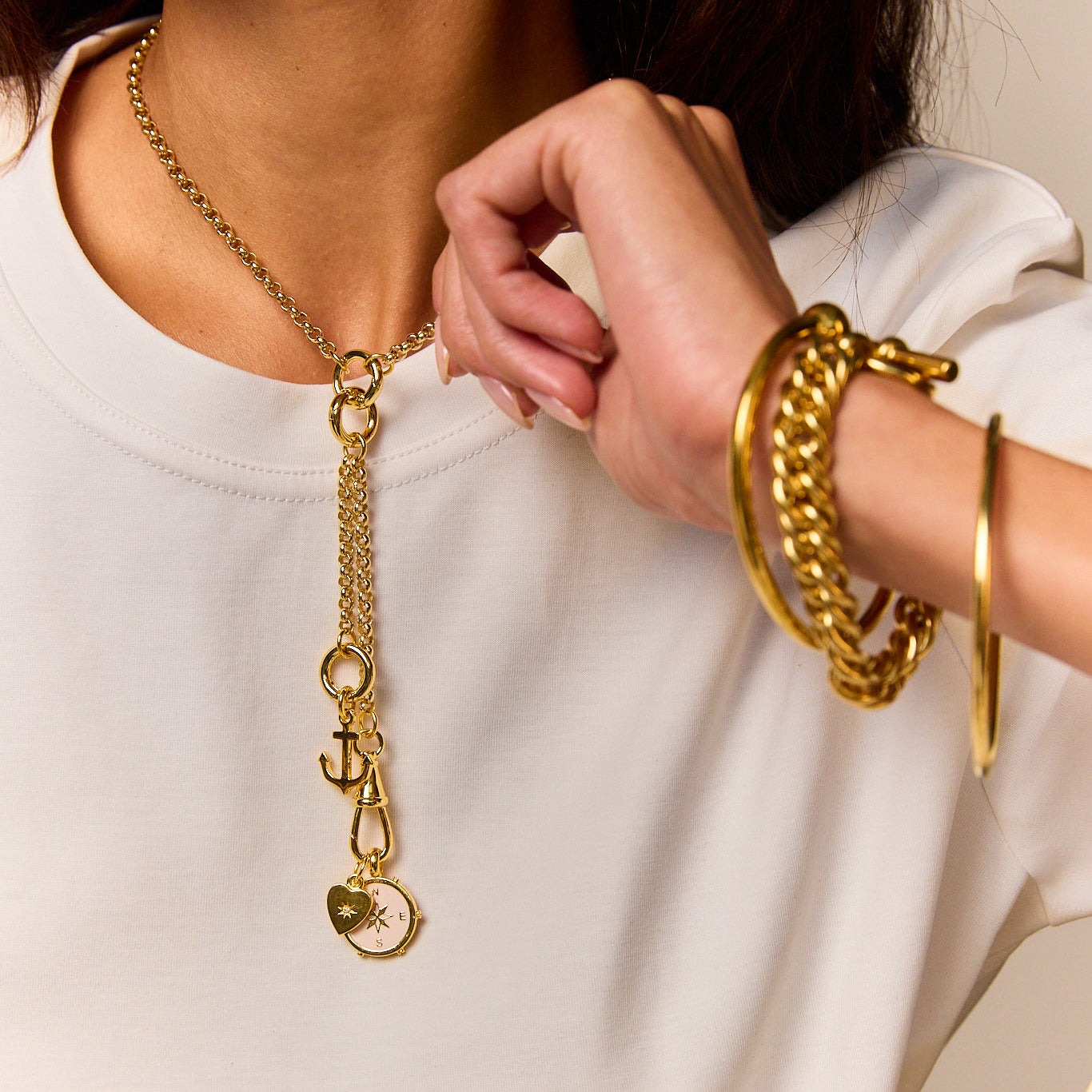 Gold charm necklace with anchor and compass pendant, worn on white crew-neck top