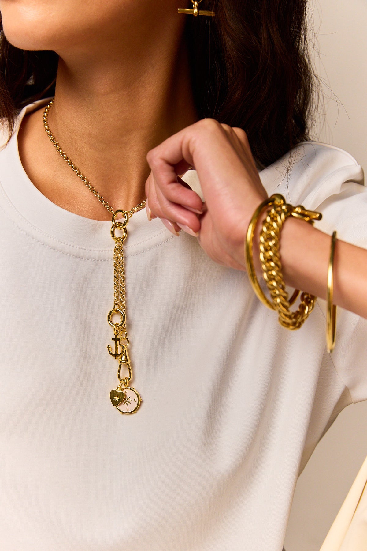 Gold charm necklace with anchor and compass pendant, worn on white crew-neck top