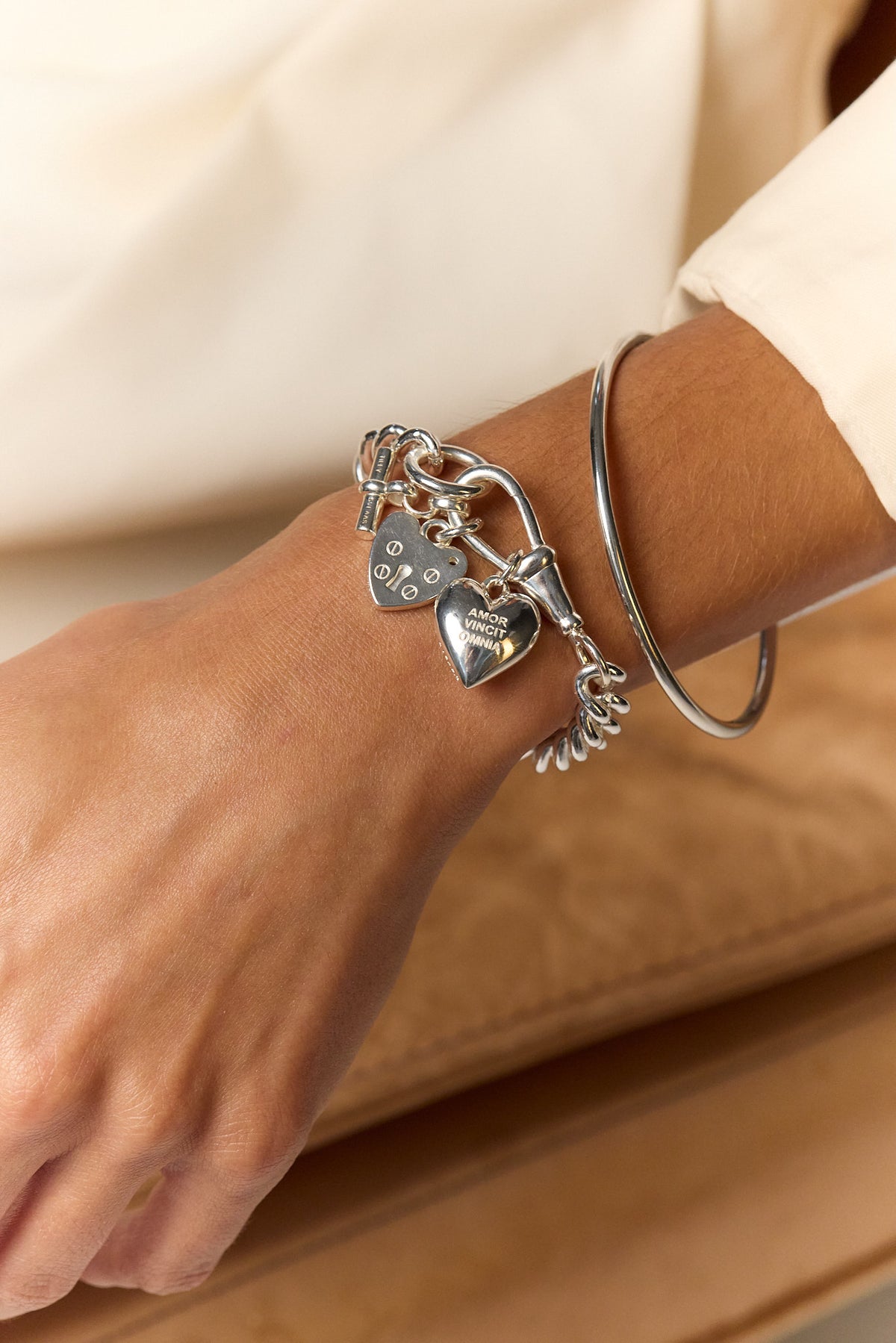 Silver charm bracelet on wrist with heart, lock, and small tag charms