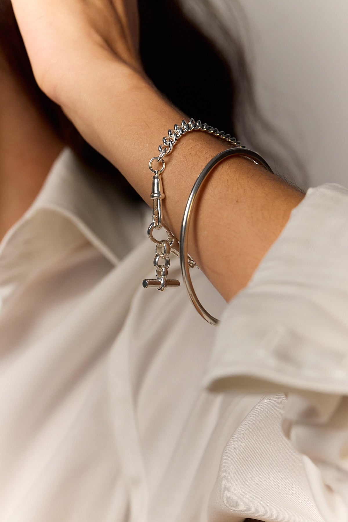Silver charm bracelet with cross and small links worn on wrist