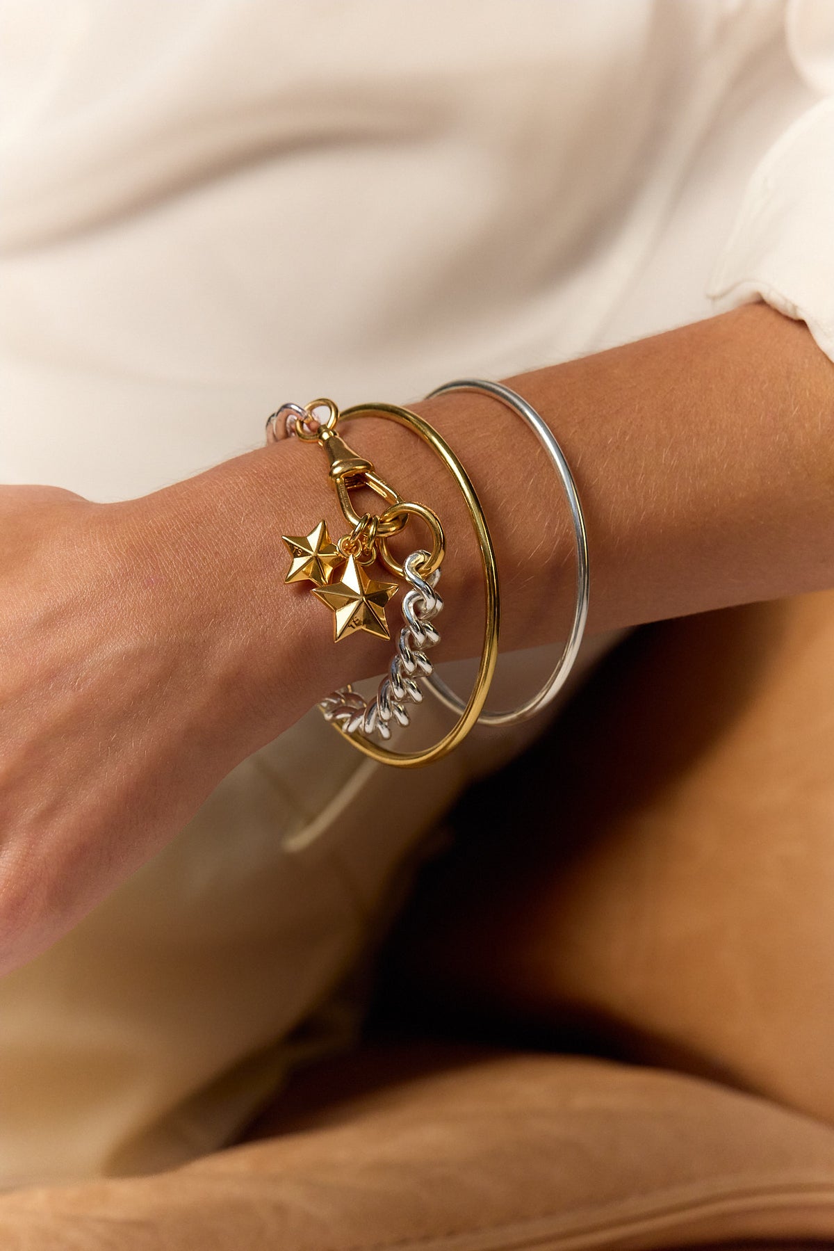 Star charm bracelet on wrist with gold and silver stacked cuffs