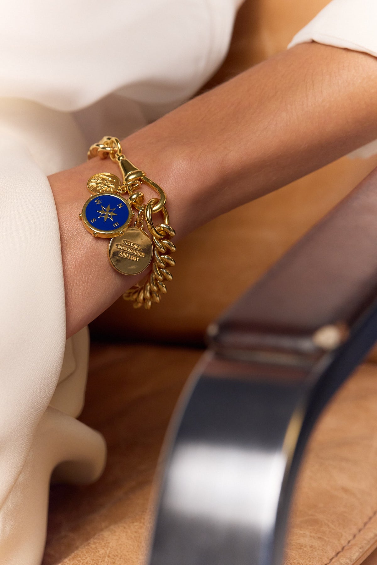 Gold charm bracelet with blue star medallion on wrist, multiple round tags