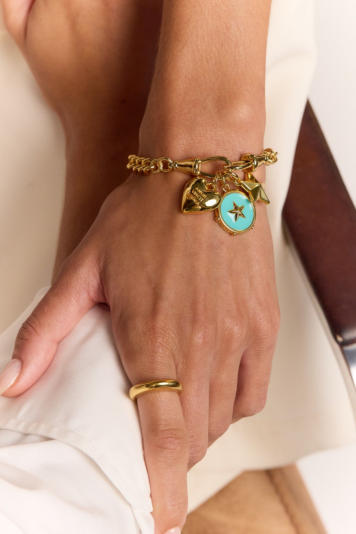Gold charm bracelet with heart, star, and blue round charm on wrist