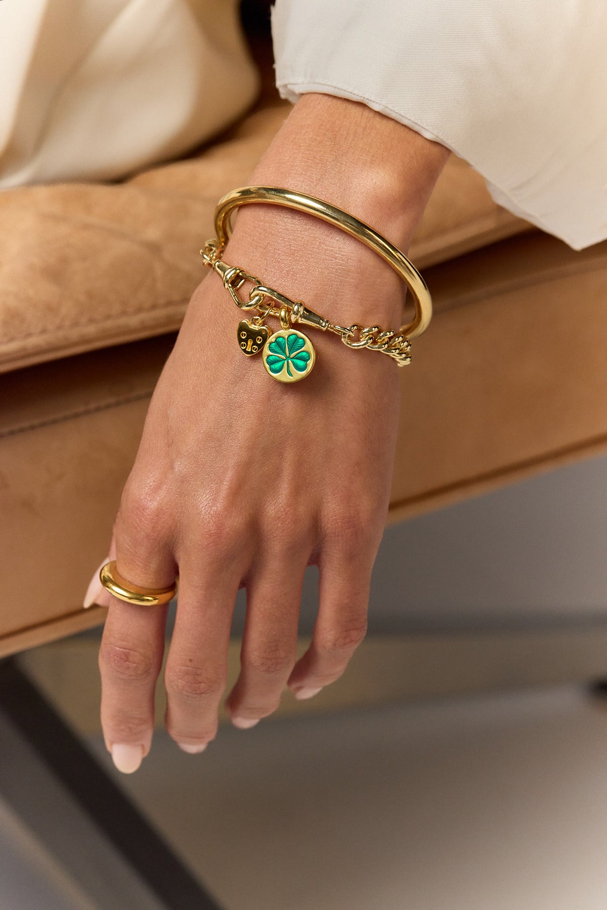 Gold-tone charm bracelet on wrist with green clover, heart padlock and chain links