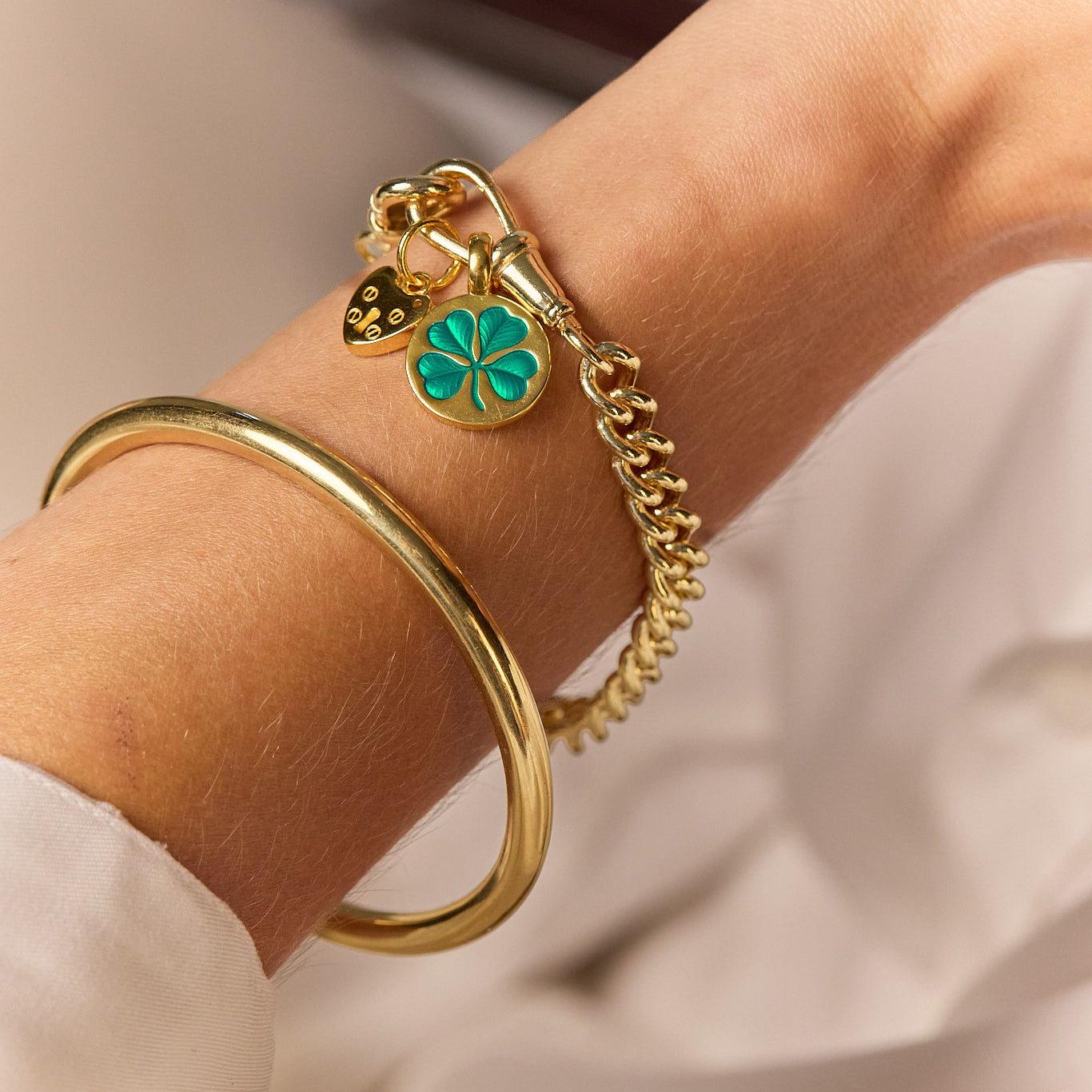 Close-up gold-tone chain bracelet with green clover charm and heart padlock