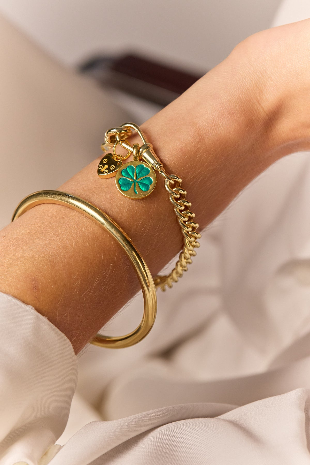 Close-up gold-tone chain bracelet with green clover charm and heart padlock
