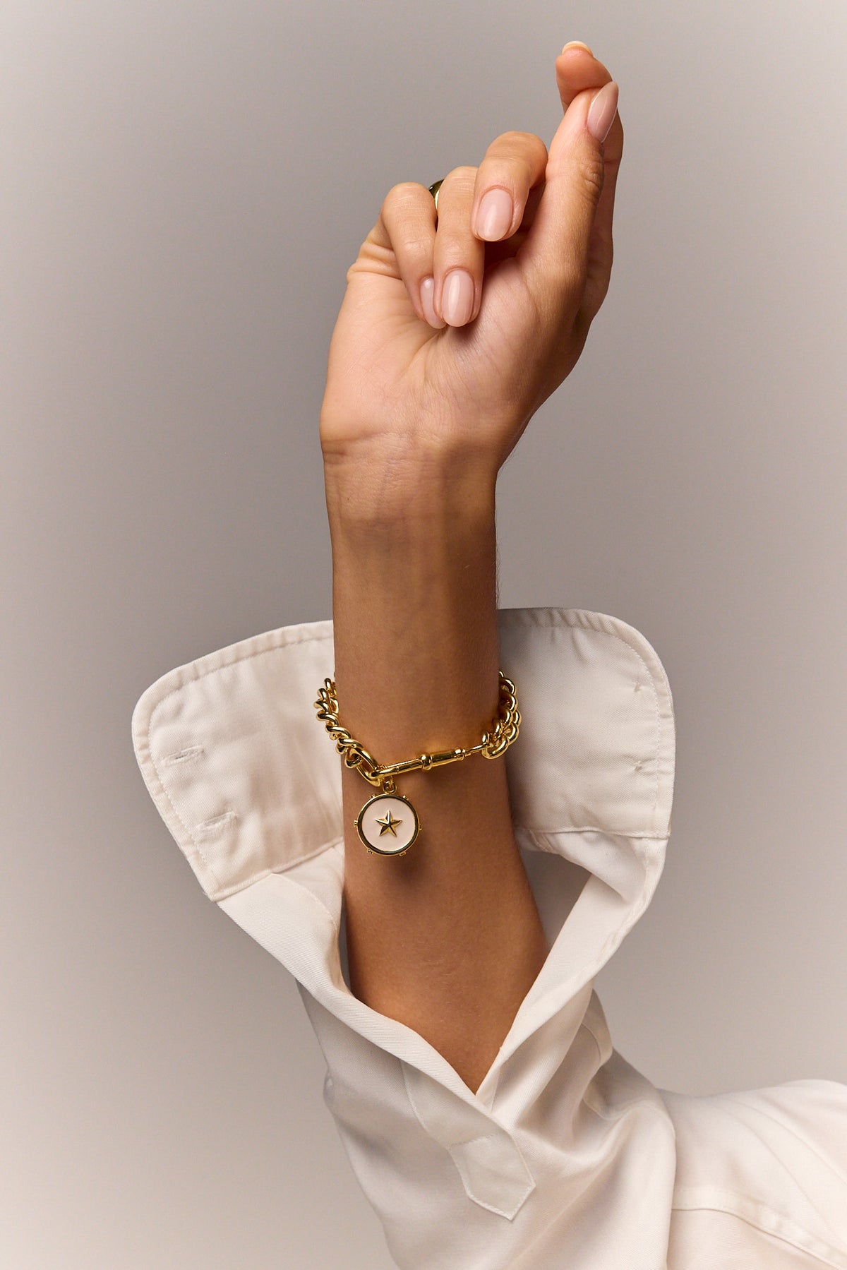 Gold chain star charm bracelet worn on wrist with white shirt