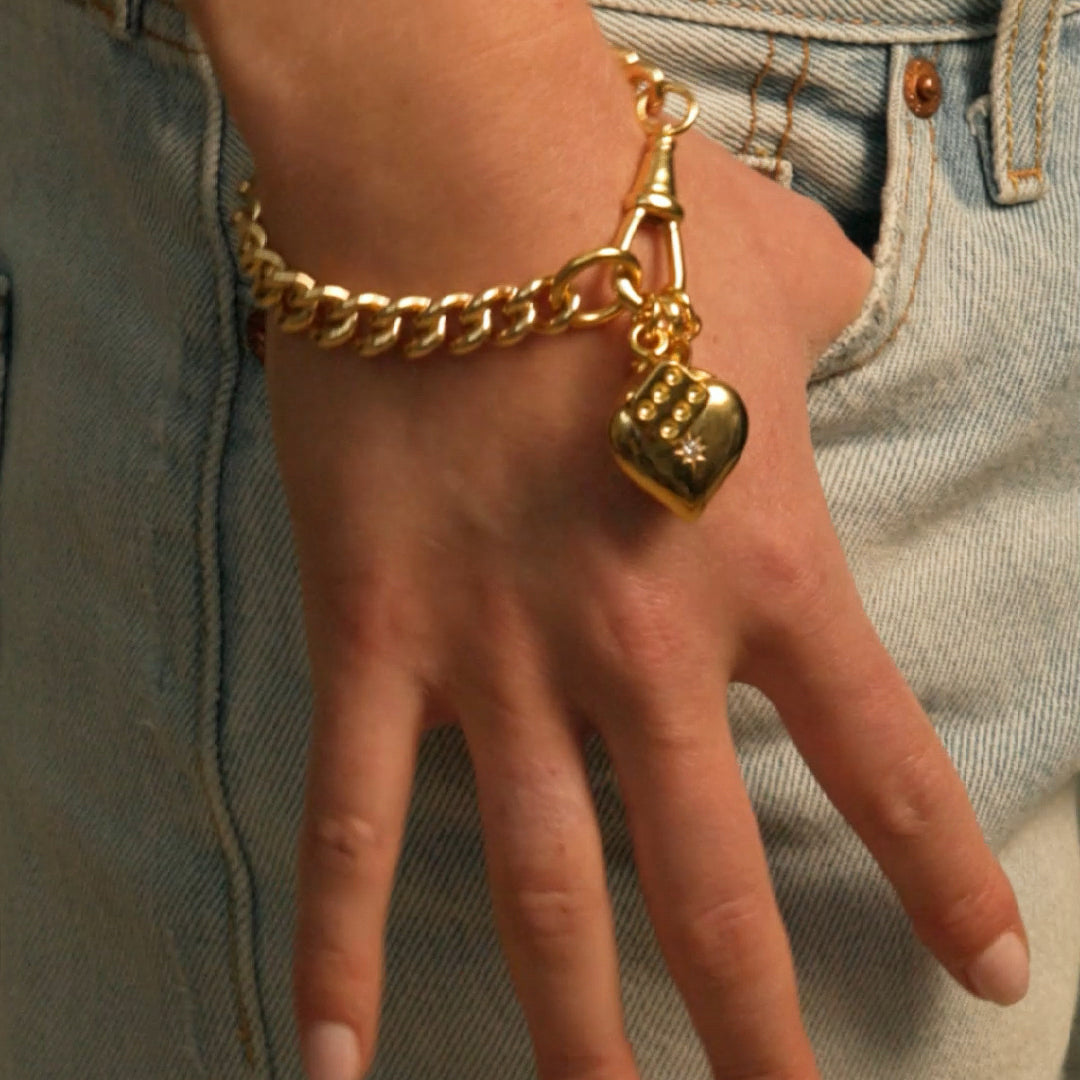 Gold curb chain bracelet with hanging heart charm on hand
