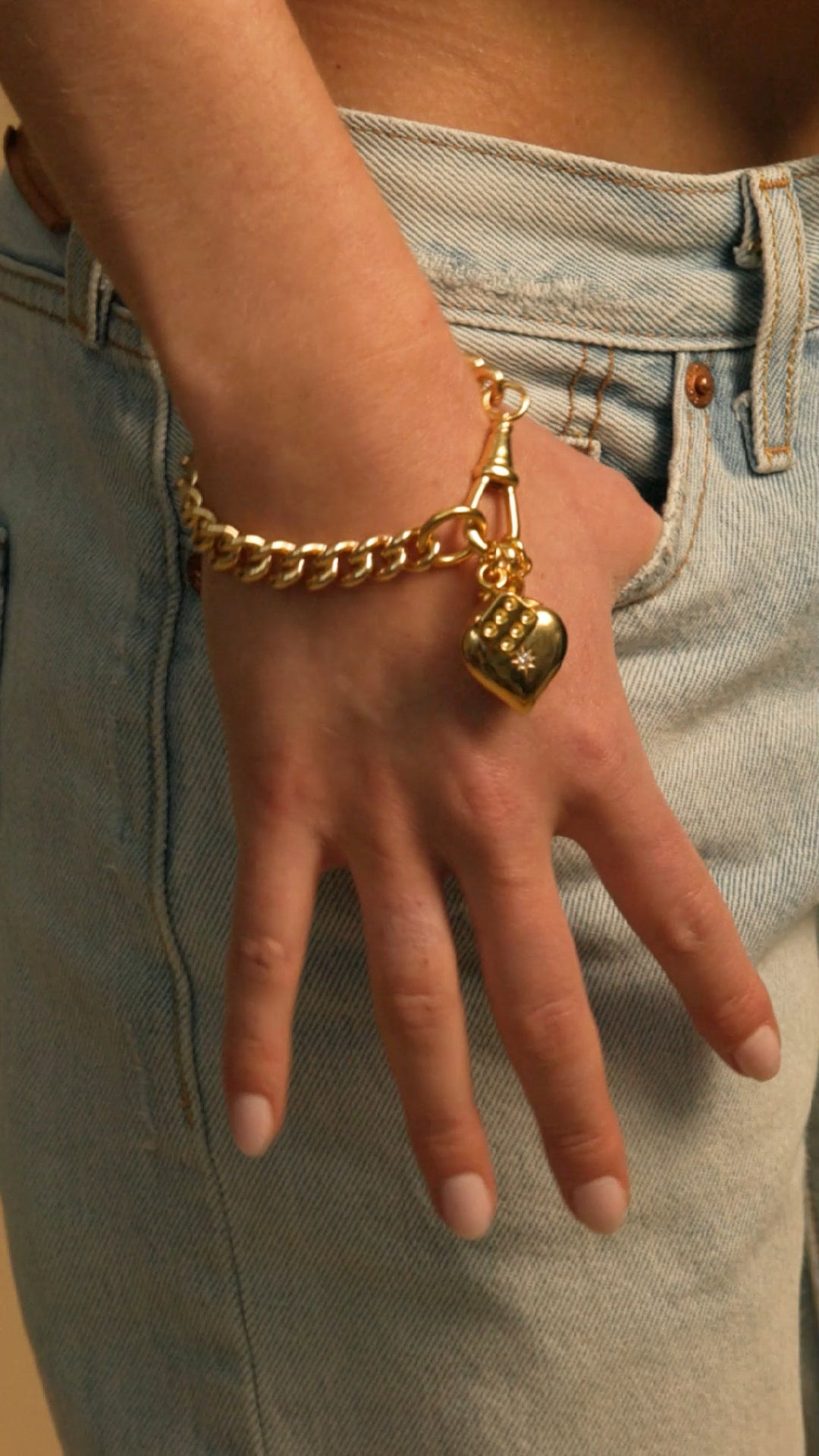 Gold curb chain bracelet with hanging heart charm on hand