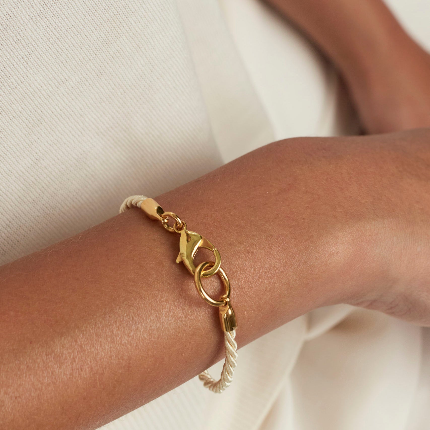Gold friendship bracelet on wrist with braided cord and ring-and-link charms