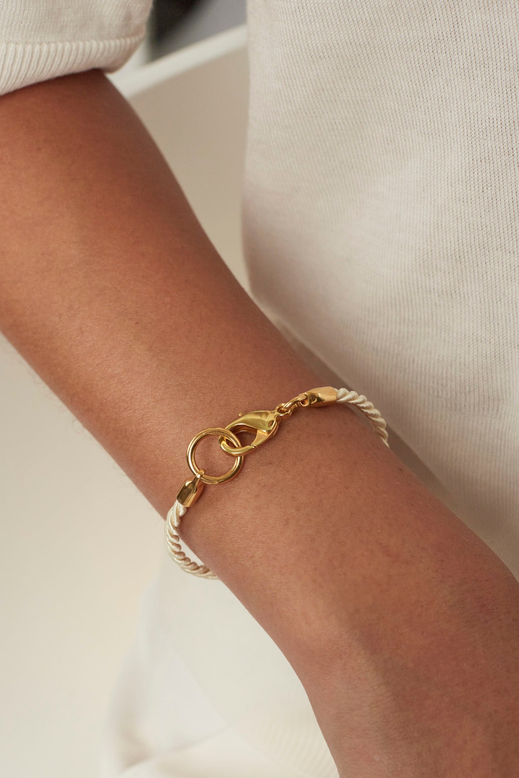 Gold friendship bracelet with braided cord and circular clasp link, worn on sleeve