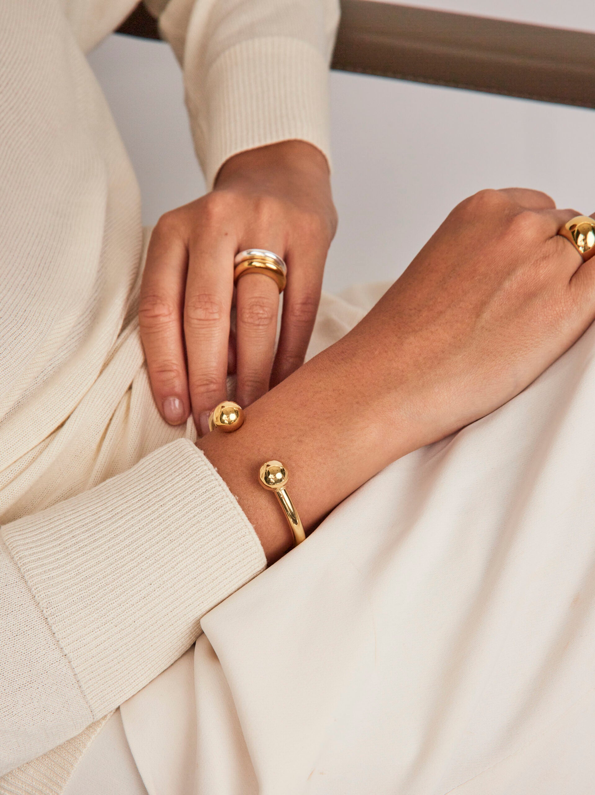 Close-up of hands wearing gold rings and a bracelet on a neutral background