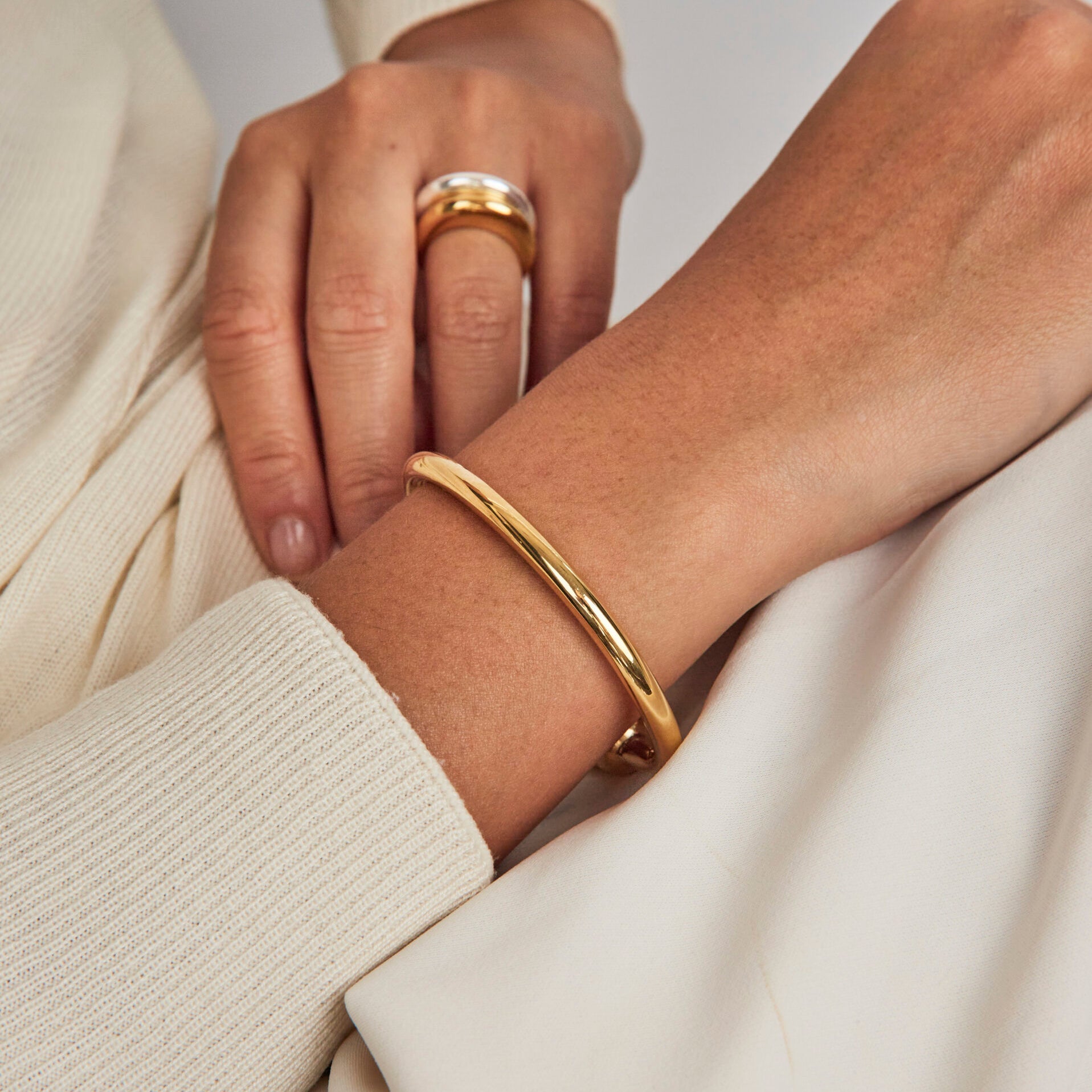 Close-up of hands wearing gold ring and bracelet on a neutral background
