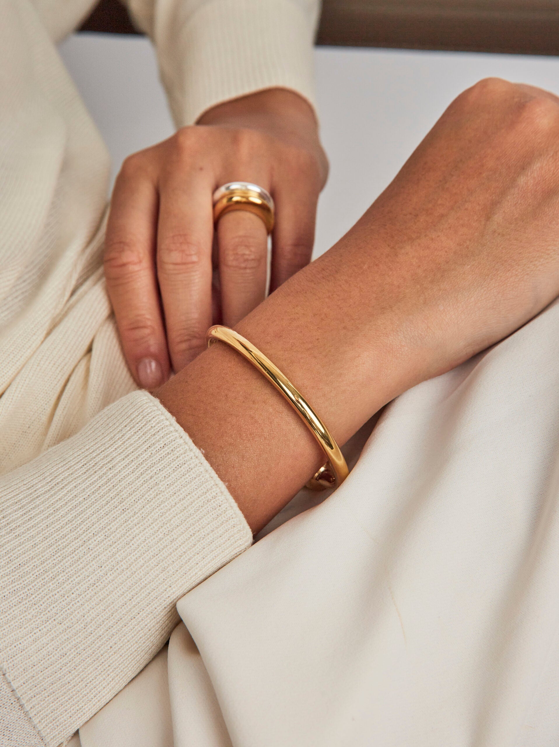 Close-up of hands wearing gold ring and bracelet on a neutral background