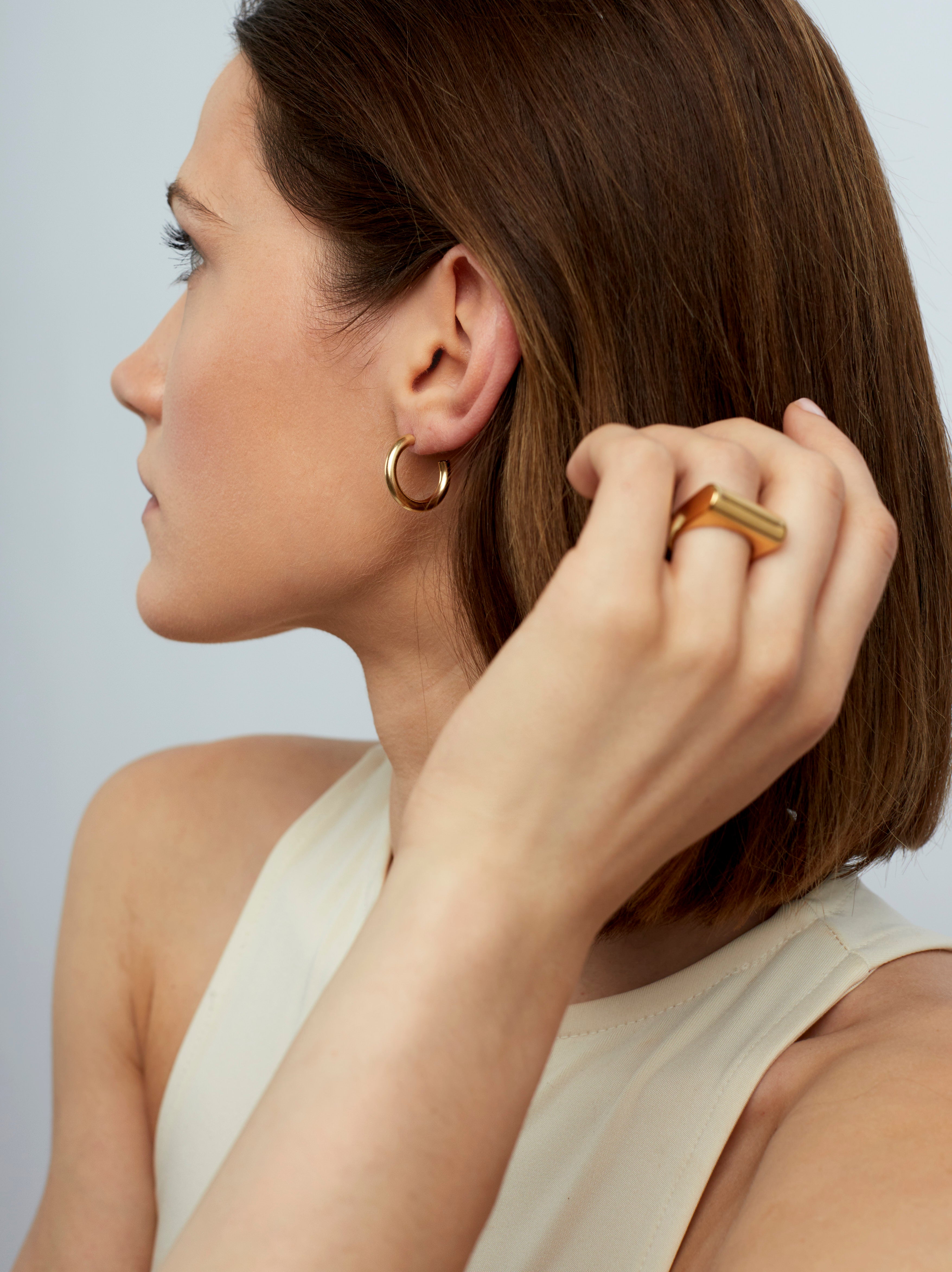 Small gold hoop earrings with hinged clasp, close view on model ear